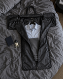 Laylowe Ellis charcoal leather garment duffle unfolded on a bed with a shirt on a hanger inside.