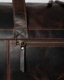 Close-up of the Laylowe Rowan dark brown leather duffle showing the front zip pocket and stitched handle attachment.