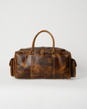 Front view of the Laylowe Alden brown leather weekender with a center buckle and pockets at both ends.