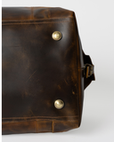 Base of the Laylowe Hayes light brown leather weekender, showing metal feet and stitched edges.