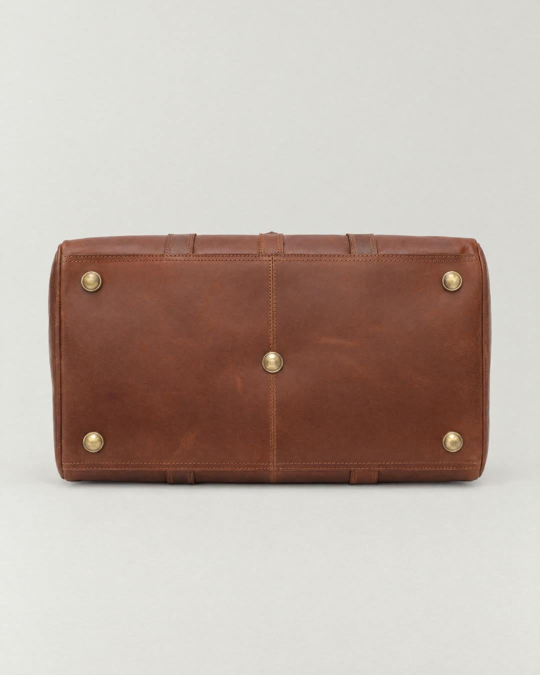 Bottom view of the Laylowe Parker tan leather weekender showing five metal feet and stitched leather panels.