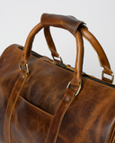 Close-up of the Laylowe Beck light brown leather duffle showing the rounded handles, metal fittings and front pocket.