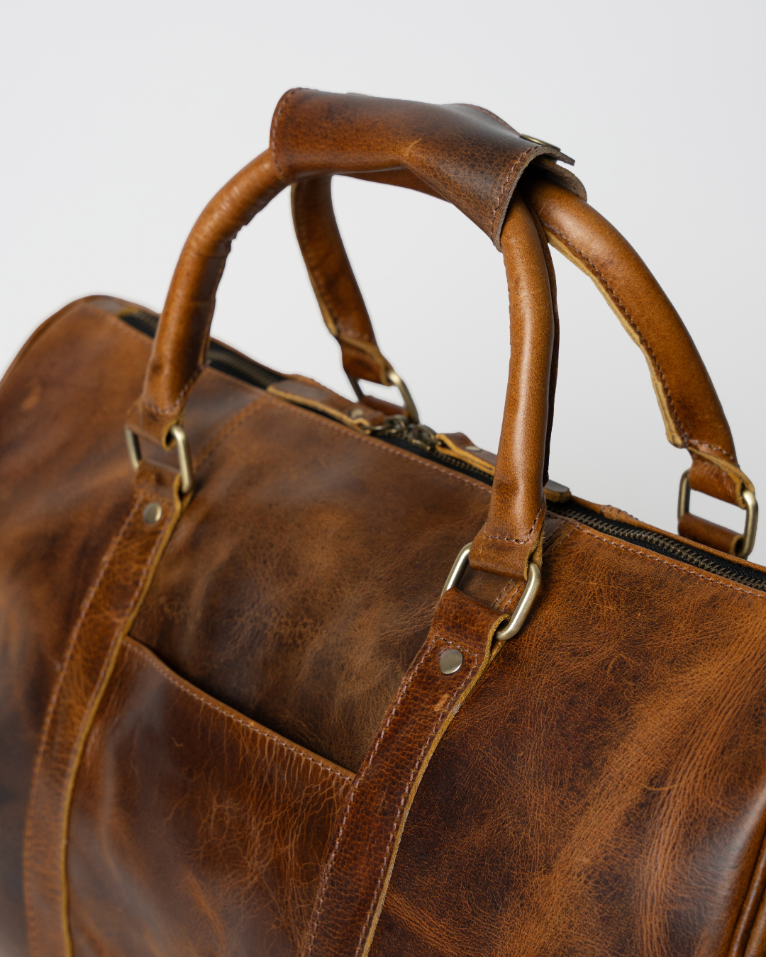 Close-up of the Laylowe Beck light brown leather duffle showing the rounded handles, metal fittings and front pocket.